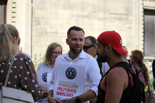 Maciej Wilk z plakatem "Odwołujemy prezydenta Warszawy" rozmawia z mieszkańcami