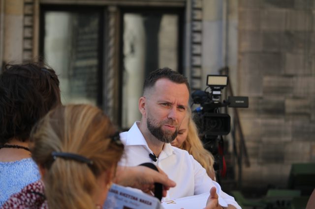 Maciej Wilk udziela wywiadu dziennikarzom przy zabytkowej fasadzie