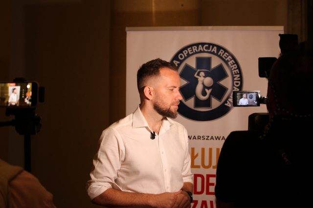 Maciej Wilk podczas nagrania wywiadu przy banerze kampanii
